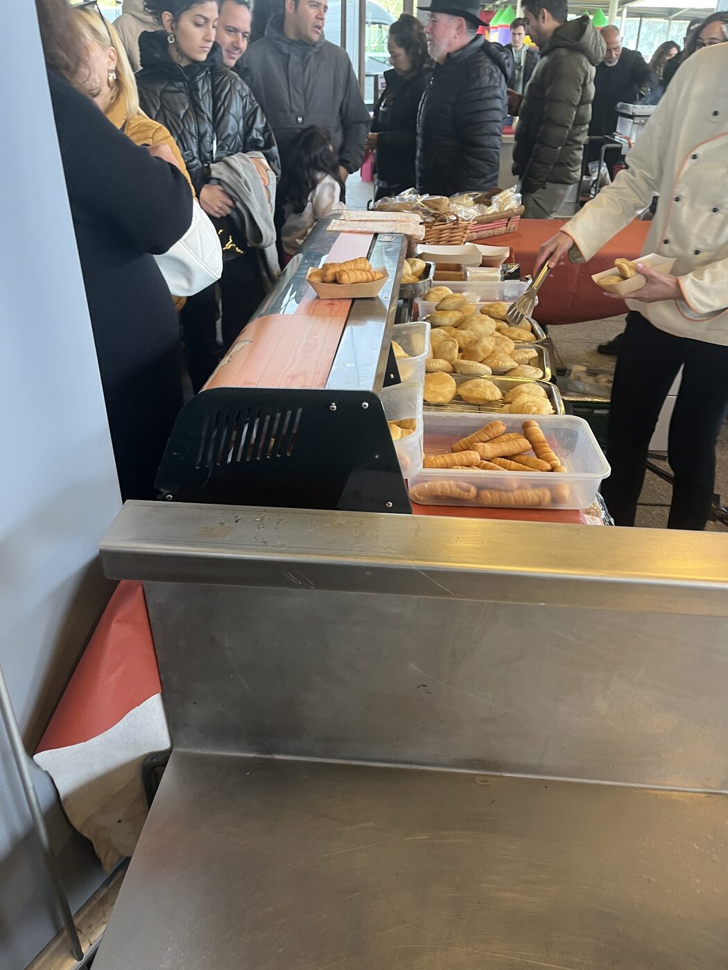Puesto de comida venezolana durante la feria, con asistentes esperando mientras se sirven productos típicos